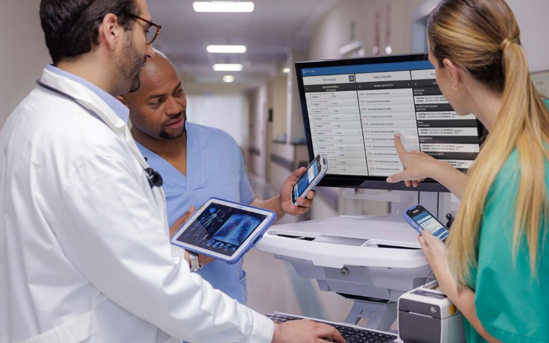 Three medical staff members discussing results from an Ergotron medical cart with Zebra mobile computers.
