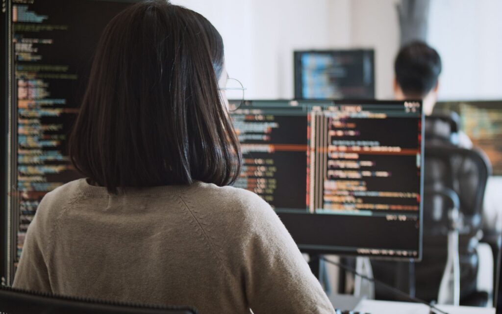 A woman sitting in front of a monitor filled with computer code